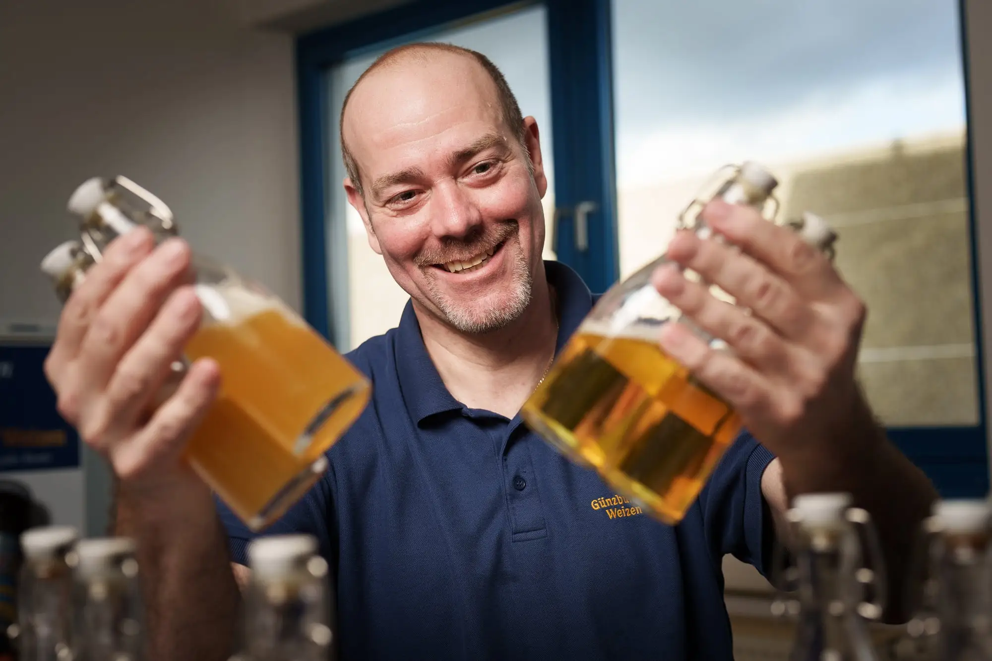 Brauer hält zwei Probeflaschen mit Weizenbier ins Licht